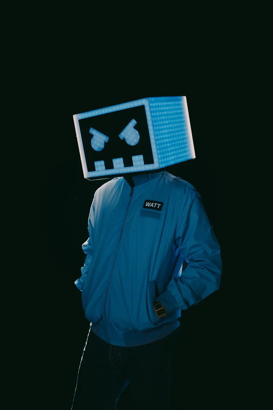 Barely Alive’s illuminated box-shaped helmet and blue jacket against a dark background.