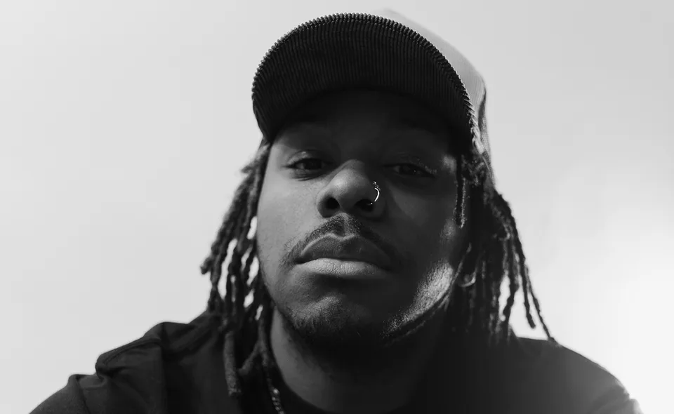 A monochrome portrait of beastboi. wearing a cap with long dreadlocks.