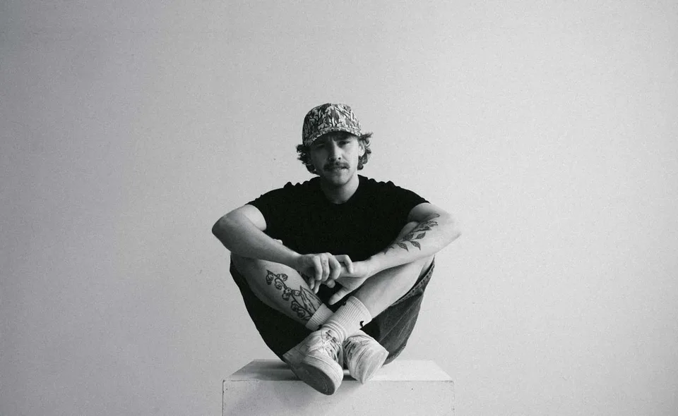 LYNY seated cross-legged in a monochrome studio portrait.