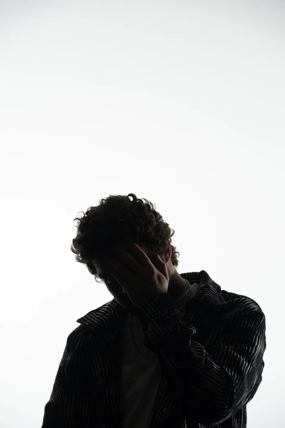 PEEKABOO with his head lowered and one hand covering his face against a light background.