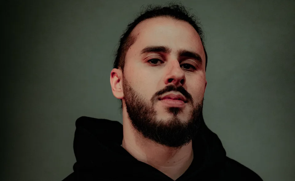 Trivecta in a dark hoodie against a green-grey background.