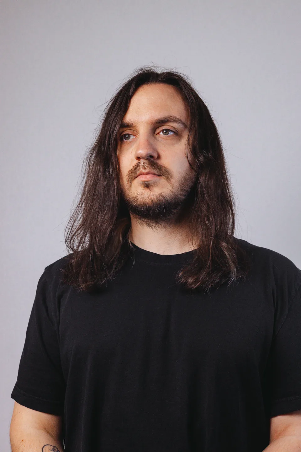 TYNAN in a black shirt against a grey studio background.